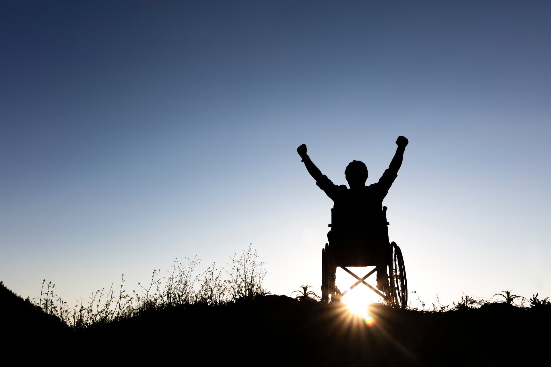 Silhouette of a person in a wheelchair raising both fists against a sunrise sky